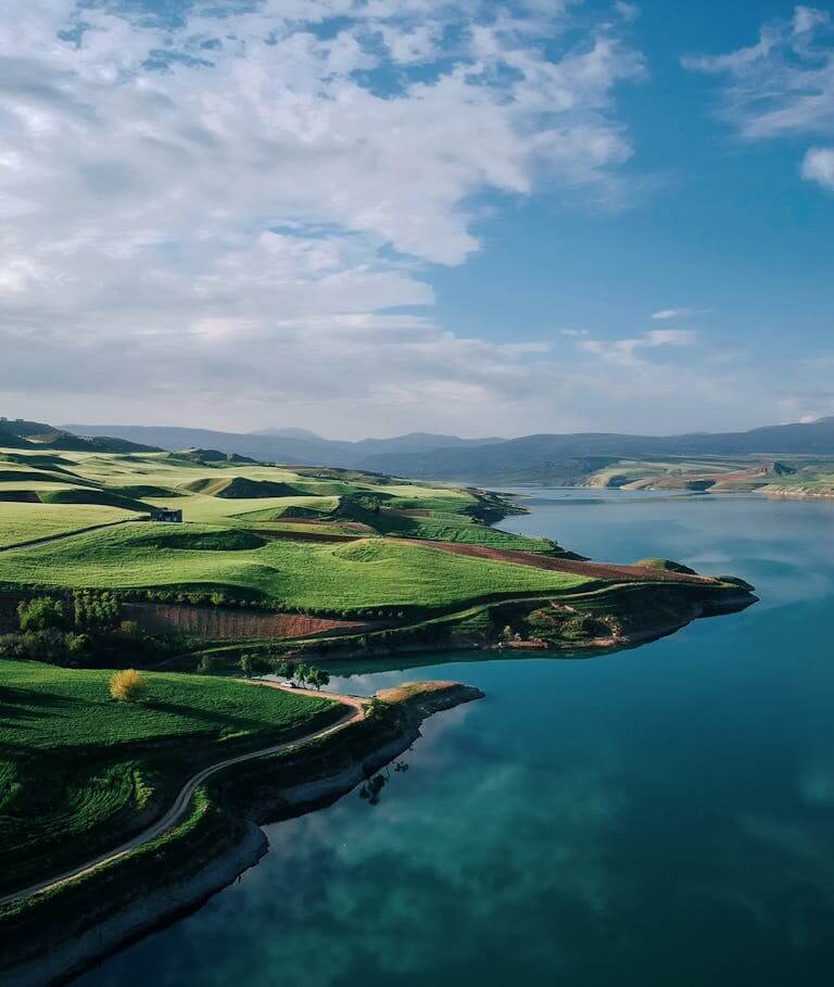 A breathtaking aerial view of vibrant green hills by a serene lake under a clear blue sky.
