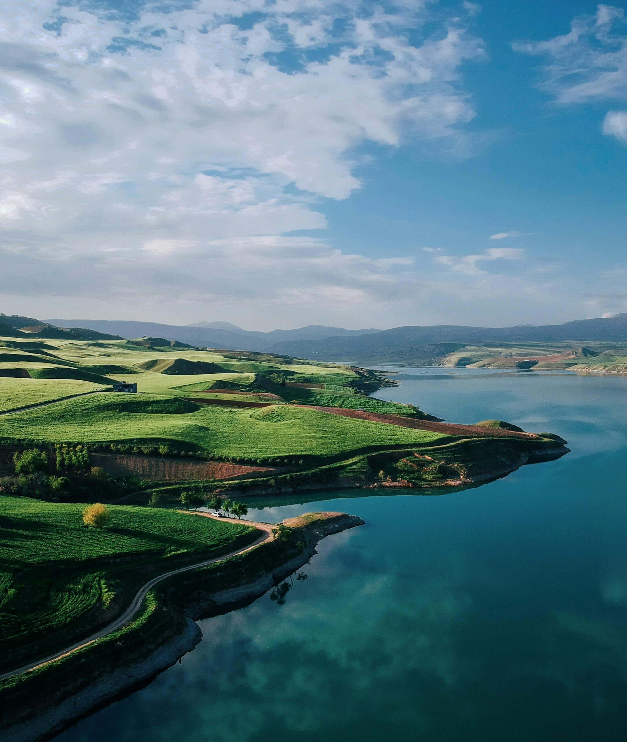 A breathtaking aerial view of vibrant green hills by a serene lake under a clear blue sky.