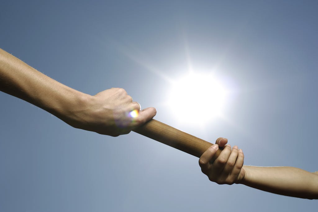 Close-up of hands passing a relay baton against a bright sunny sky.