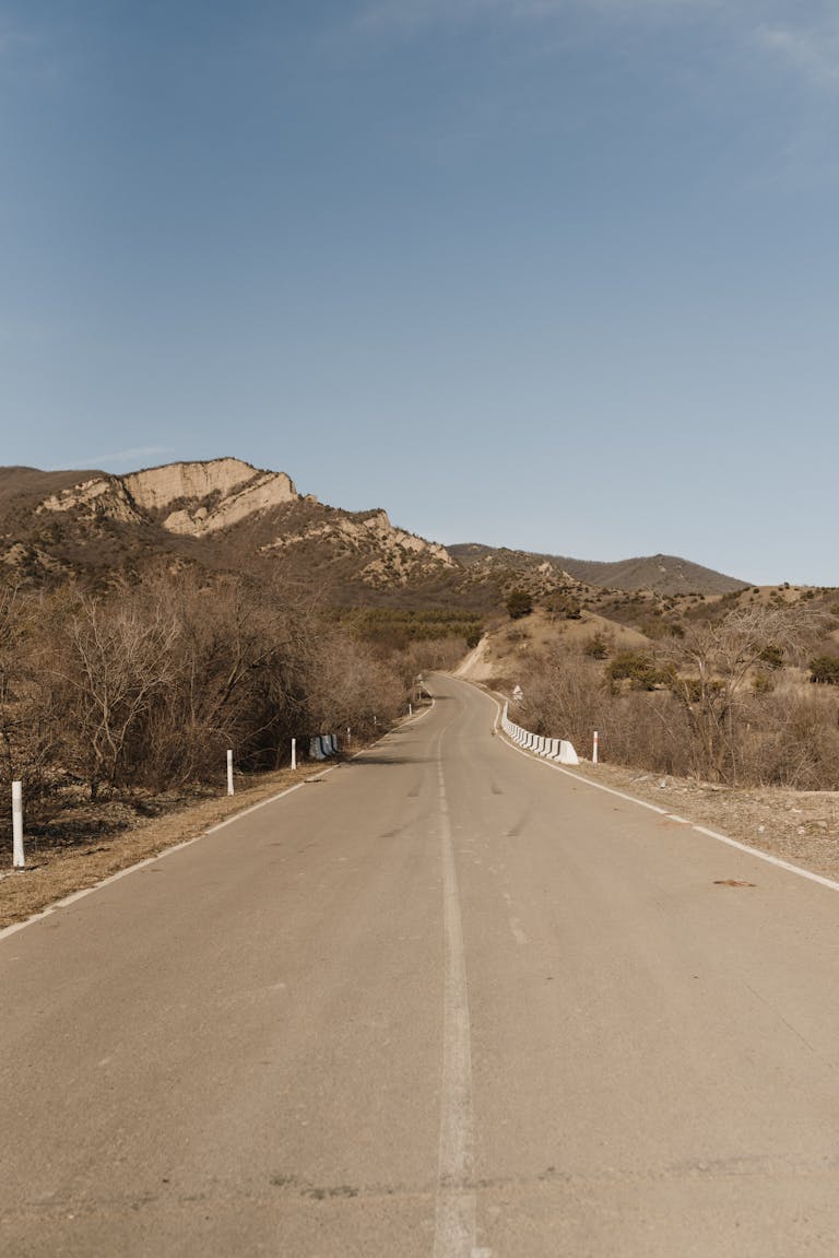 Empty rural road leading towards majestic mountains under a clear blue sky.